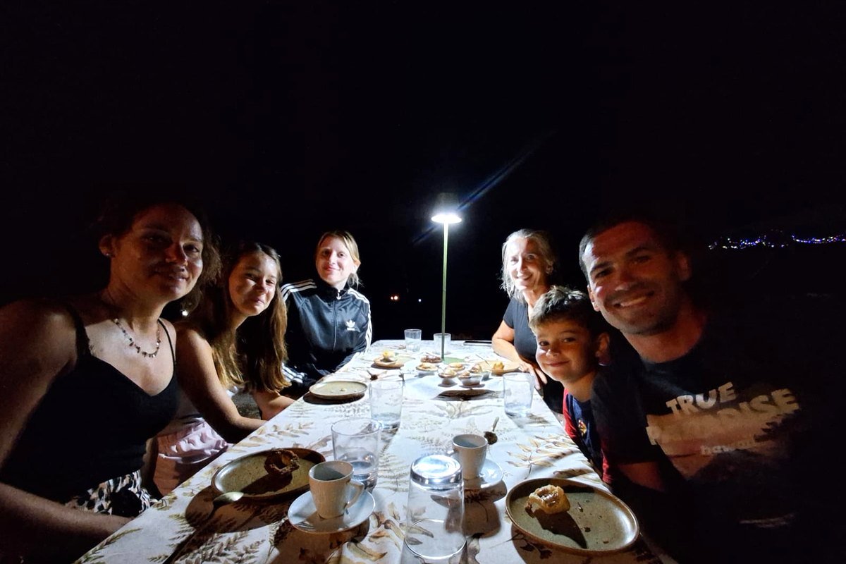 Volontari e vicini a cena attorno a un lungo tavolo all’aperto, di sera